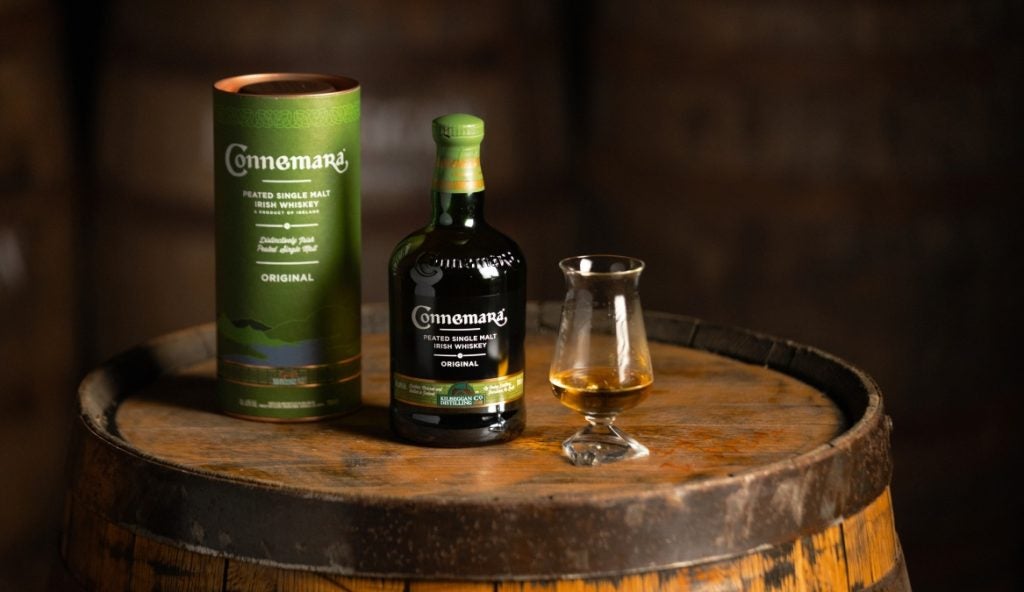 A bottle of Connemara Peated Single Malt next to a glass and gift box on a barrel with dark tones