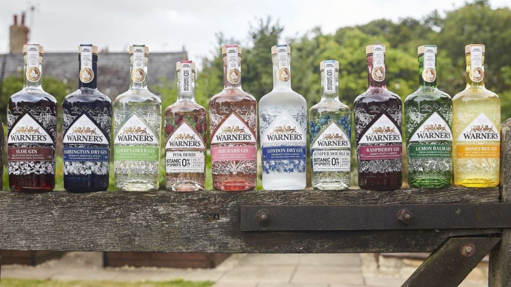 range of spirits bottles on wooden gate, outdoors, leafy background.