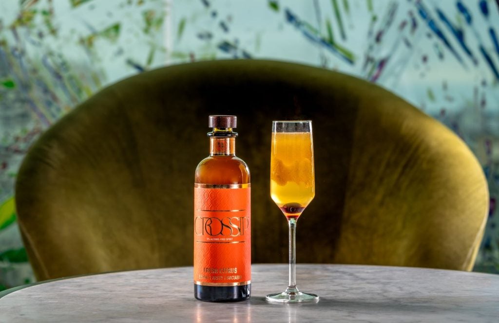 orange bottle with orange Crossip label next to cocktail in flute glass.